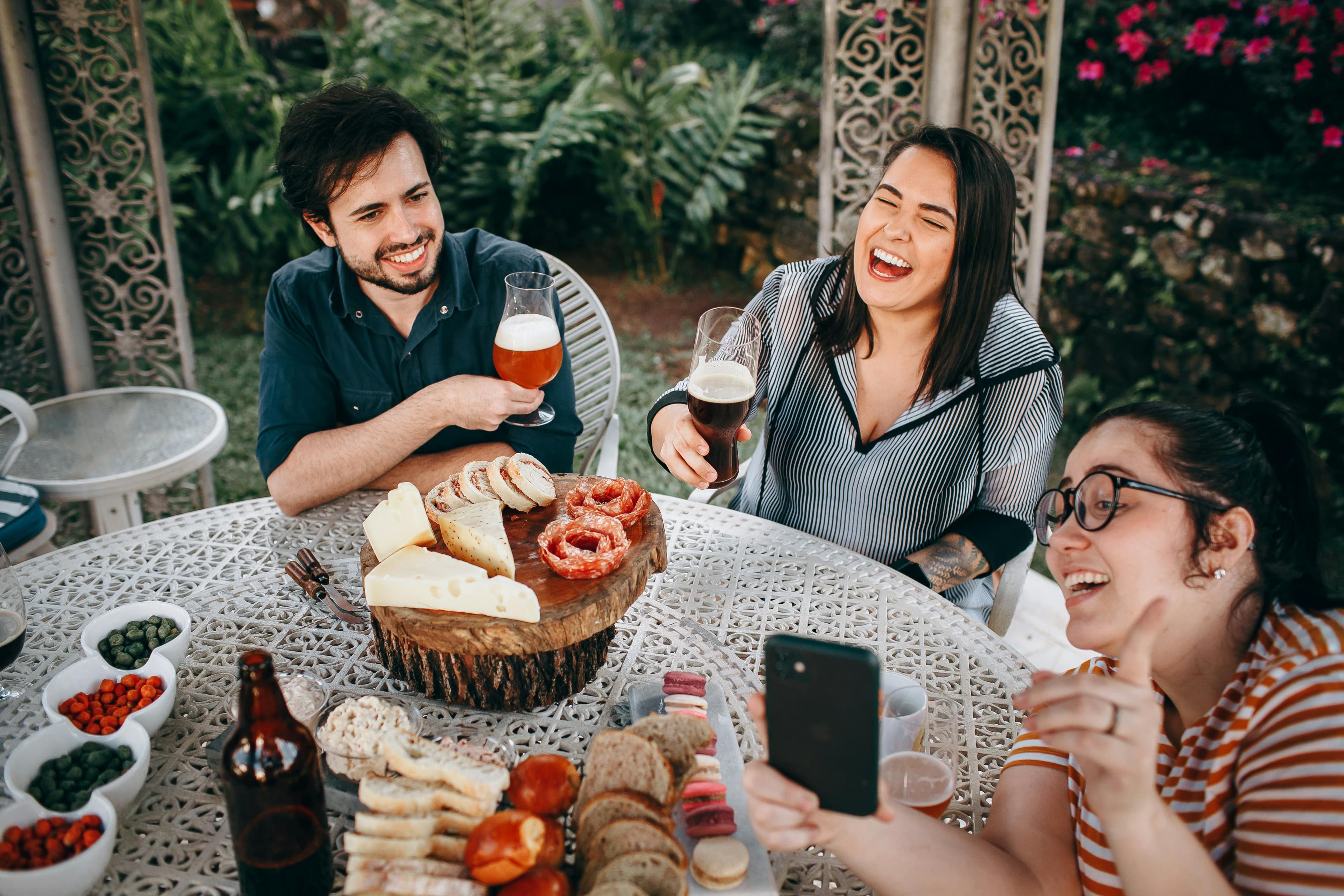 Friends laughing around an outdoor table with charcuterie and beer