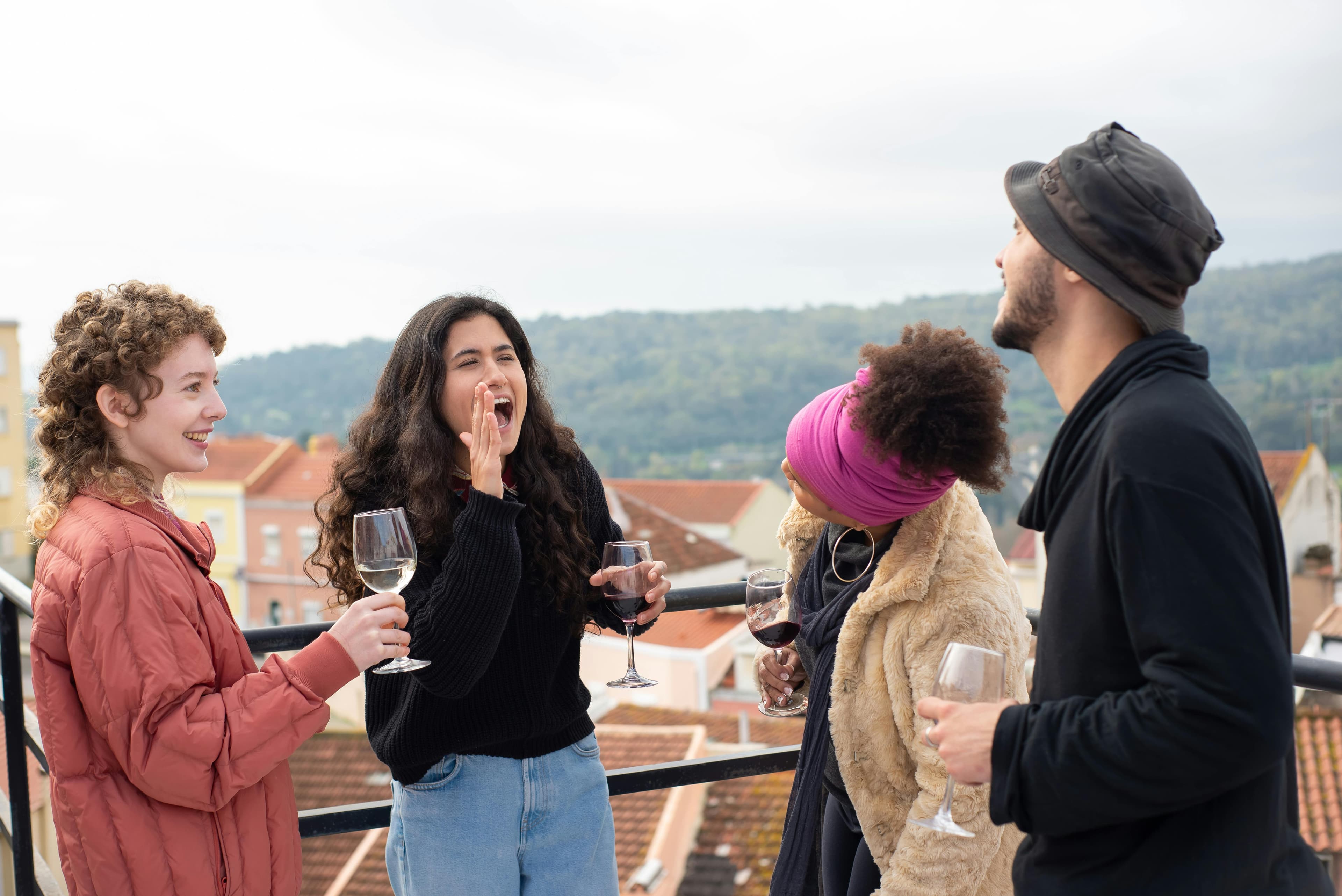 Two crews on a hilltop terrace with wine in cool weather, terracotta rooftops behind